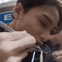 a close up of a person eating with chopsticks in front of a blue sign that says e