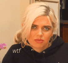 a blonde woman wearing a black hoodie has the word wtf on her shoulder
