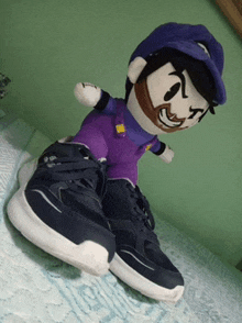 a stuffed mario wearing a purple shirt and hat is sitting on a pair of shoes
