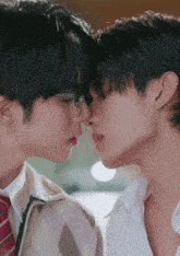 two young men kissing with one wearing glasses and the other wearing a tie