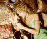 a woman in a green dress is laying on a bed holding a guitar