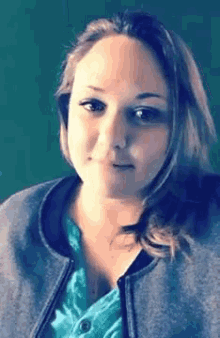 a woman wearing a gray jacket and a blue shirt is making a face .