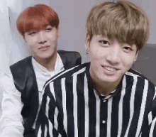 two young men are sitting next to each other and smiling . one of the men is wearing a striped shirt .