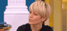 a woman with short blonde hair is sitting in front of a white pillar .