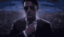 a man in a suit and tie with blood on his shirt is adjusting his tie .