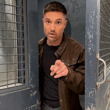 a man in a brown jacket is pointing his finger at the camera