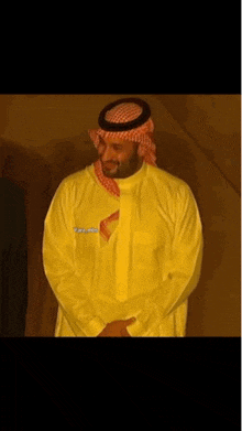 a man wearing a yellow shirt and a red head scarf stands with his hands folded