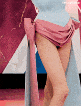 a woman in a blue dress with a pink sash around her waist is standing on a red carpet .