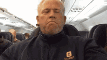 a man is sitting on an airplane wearing a jacket with the letter g on it