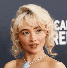 a woman with blonde hair and blue eyes is wearing a blue necklace