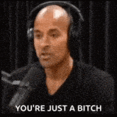 a bald man wearing headphones is talking into a microphone and says `` you 're just a bitch '' .