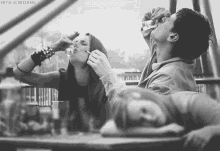 a black and white photo of a man drinking from a bottle and a woman smoking a cigarette