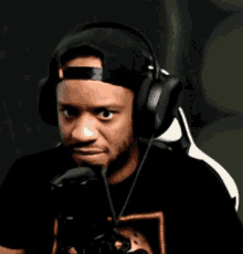 a man wearing headphones and a baseball cap is sitting in front of a microphone and making a funny face .