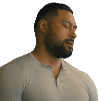 a man with a beard wearing a grey shirt looks down with his eyes closed