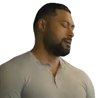 a man with a beard wearing a grey shirt looks down with his eyes closed