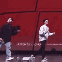 two men are playing badminton on a stage with a red wall in the background .