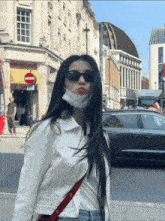 a woman wearing sunglasses and a mask stands on a street