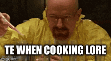a man with a beard and glasses is sitting at a table with a spoon in his mouth and a yellow jacket .