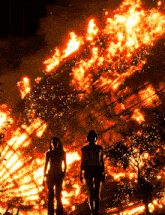 two people are standing in front of a huge fire
