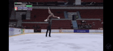 a female figure skater is doing a trick on the ice with a scoreboard behind her that says 3