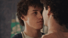 a man with curly hair is kissing another man on the cheek