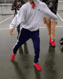 a man in a white hoodie and blue pants is dancing on a tennis court .