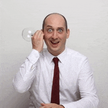 a man wearing a white shirt and a red tie is holding a light bulb to his ear