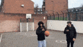 a man holding a basketball on a basketball court while another man looks at his phone