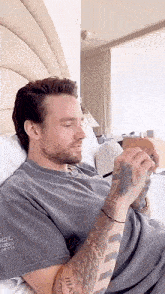 a man with a beard is laying on a bed looking at his cell phone .