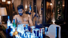 a shirtless man standing in front of a bar full of bottles and glasses