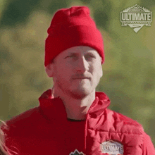 a man wearing a red beanie and a red jacket is standing in front of a forest .