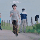 a man in a grey shirt is running down a dirt road with other people