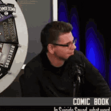 a man is sitting in front of a microphone with a comic book in the background