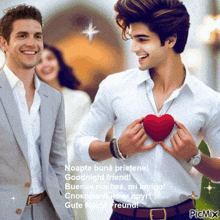 a man in a suit holds a red heart while another man stands behind him