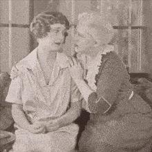 two women are sitting next to each other and one is whispering into the other 's ear