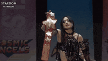 a woman holding a wrestling belt in front of a sign that says cosmic cels