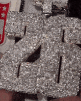 a person is holding a necklace with the number 26 covered in diamonds