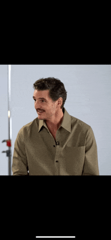 a man in a green shirt with a mustache is standing in front of a white wall