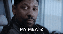 a man with a beard is sitting in a car with the words my meatz written on his face .