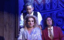 a man in a suit and tie stands next to a woman in a silver dress and a man in a red suit