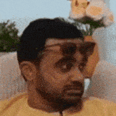 a man wearing sunglasses is sitting on a couch with a vase of flowers in the background .