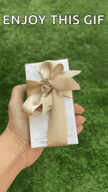 a person is holding a gift box with a bow and the words enjoy this gif above it