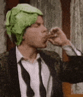a man in a suit and tie is wearing a cabbage hat and eating a piece of meat .