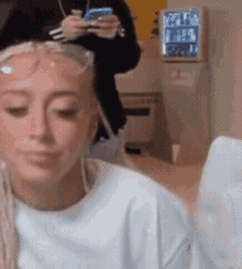 a woman wearing sunglasses is sitting in a room with a man holding a cell phone in the background .