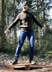 a man in a sweater and hat balances on a balance board in the woods