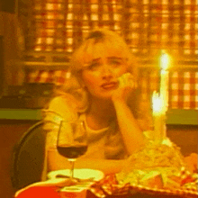 a woman is sitting at a table with a glass of wine and a candle