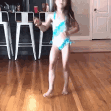 a little girl in a blue and white swimsuit is dancing on a hardwood floor