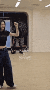 a woman in a black crop top and wide leg jeans is dancing in a room with the word story on the floor