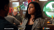 a woman in a plaid jacket is talking to a man while holding a martini in front of a chicago fire sign