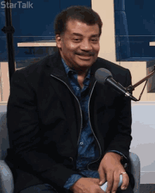 a man in a black jacket sits in front of a microphone with startalk written on the bottom right